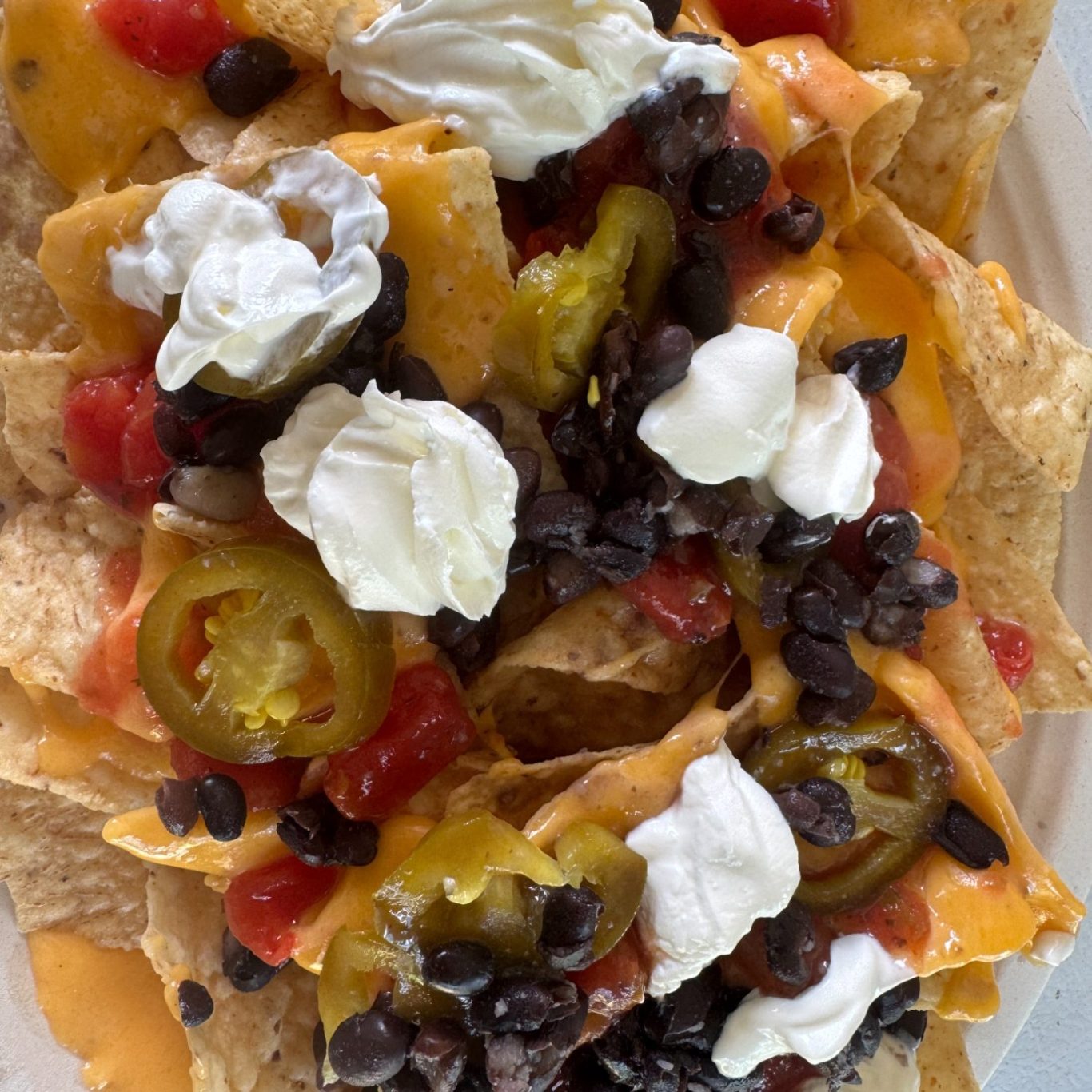 Nacho Supreme Plate of nachos topped with cheese, sour cream, black beans, jalapeños, and diced tomatoes.